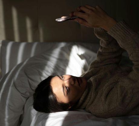 A woman lying in bed and looking at her phone with a soft smile.